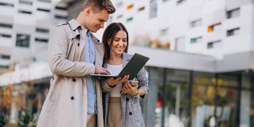 Young couple standing together outside and using computer